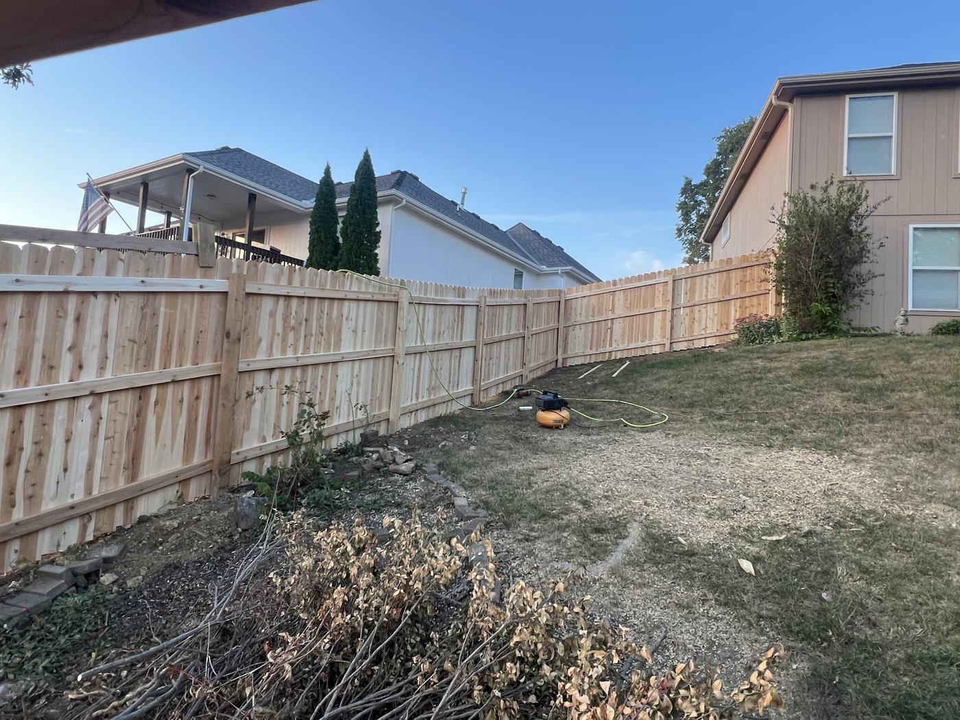 Cedar privacy fence in a back yard with a compressor still on the grass