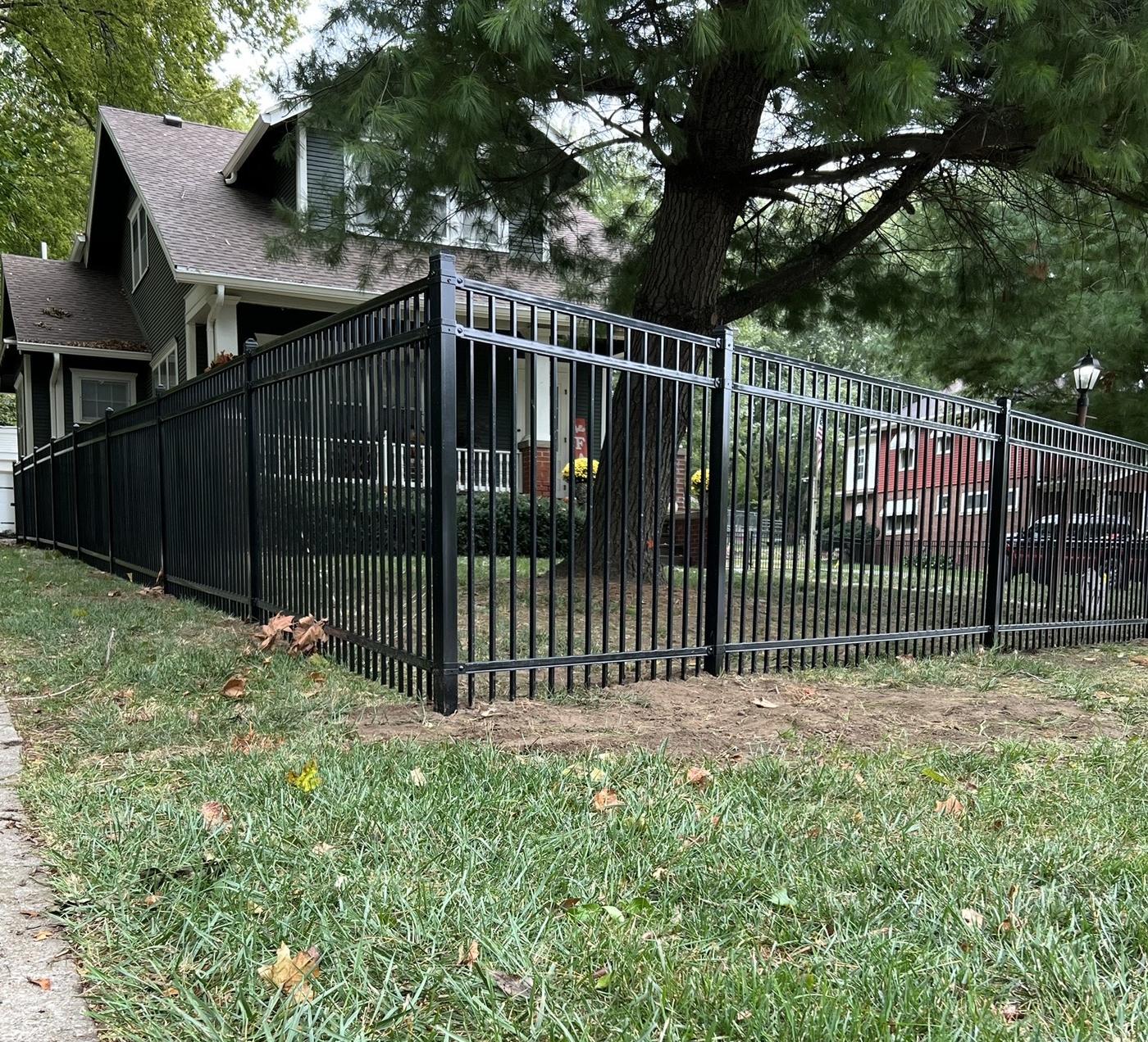 Black ornamental fence running along a mature front yard past a craftsman house