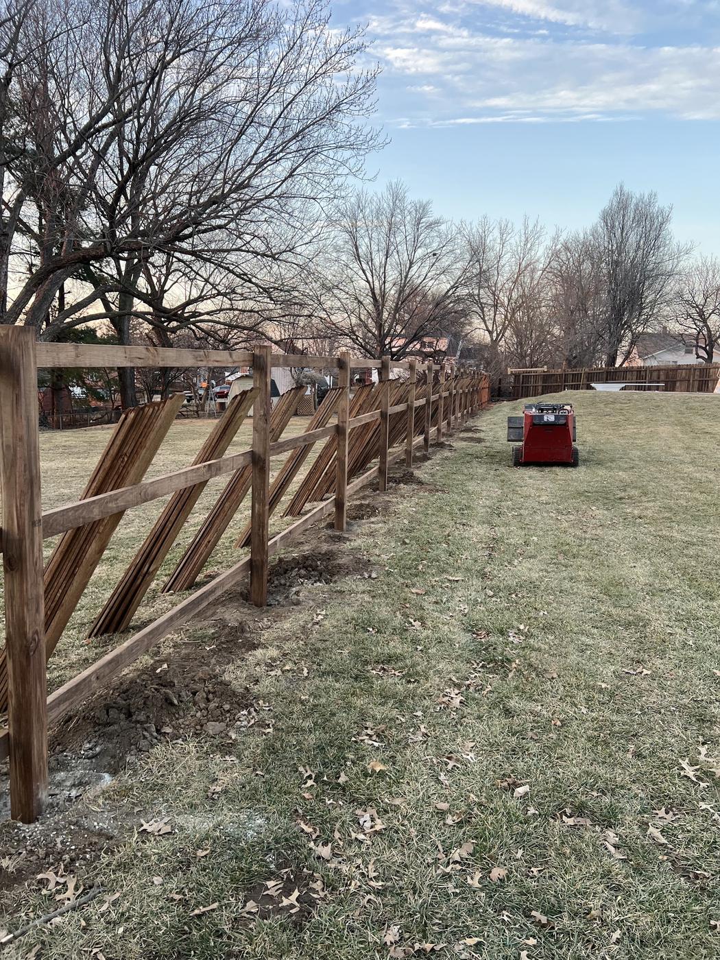 Fence posts and rails set with pickets stacked ready to hang, and a tracked machine on site