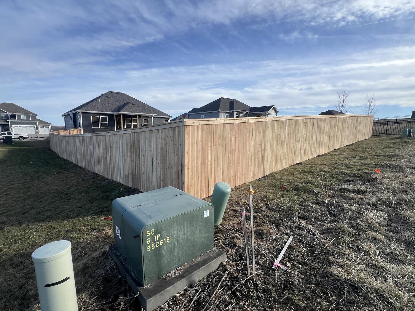 A long run of new cedar privacy fence curving around a new-build lot